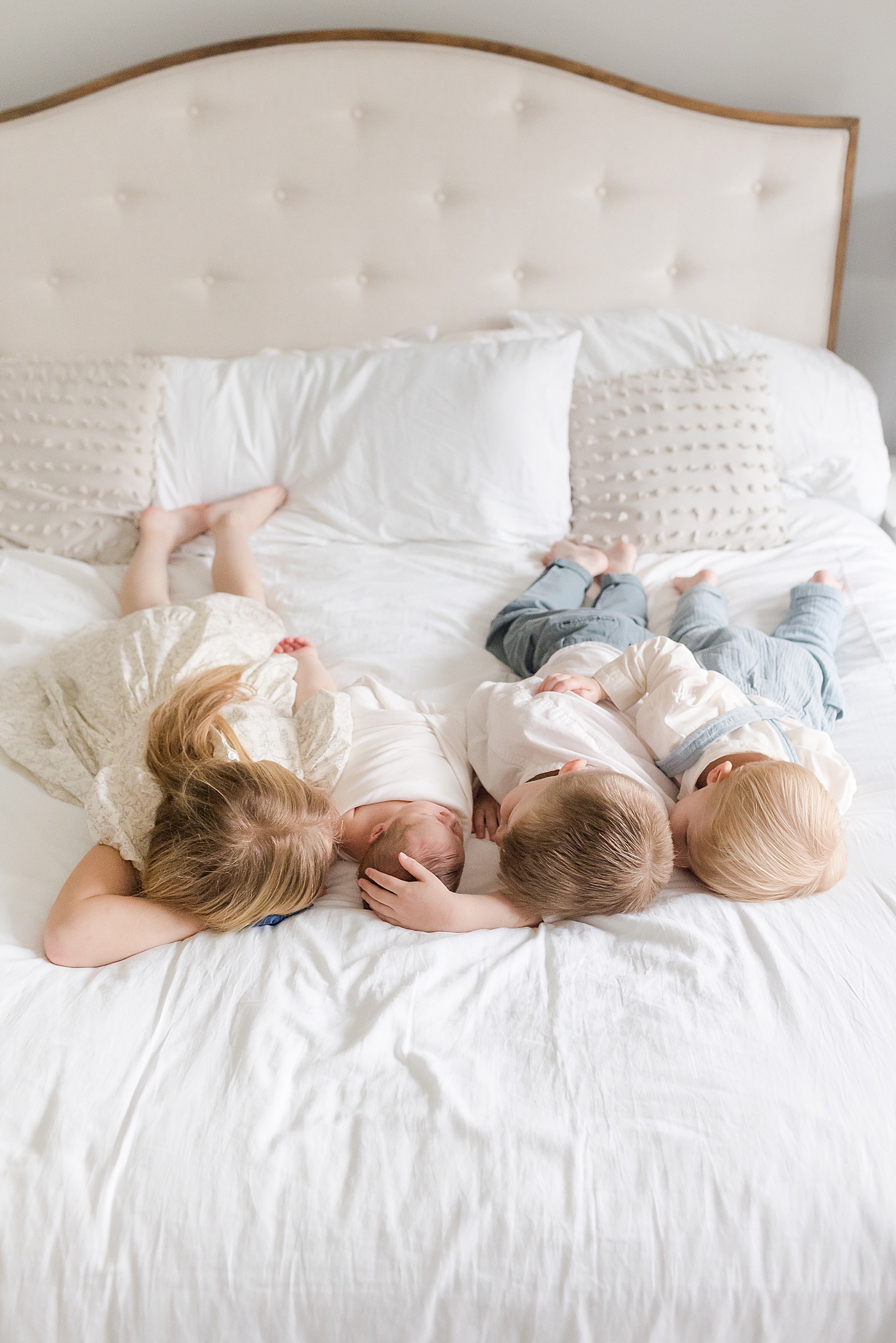 Siblings laying on a bed with their new baby | Image by Emily Gerald Photography