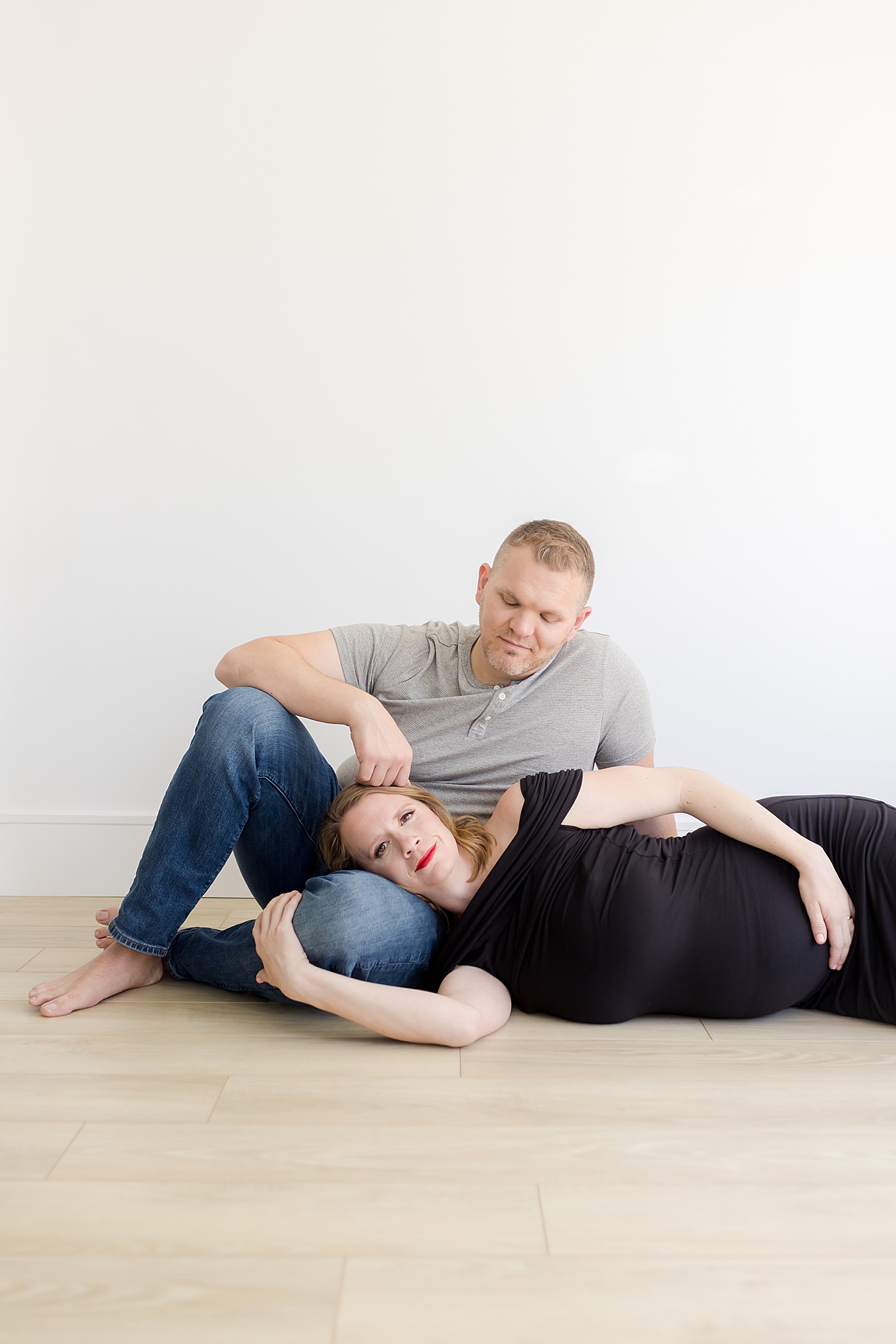 Mom and dad to be laying on the floor of the studio during maternity photos | Image by Emily Gerald Photography